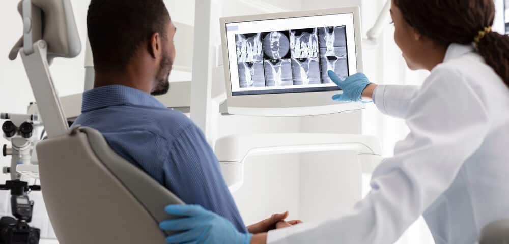 African,Female,Dentist,And,Male,Patient,Watching,Xray,On,Digital