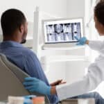 African,Female,Dentist,And,Male,Patient,Watching,Xray,On,Digital